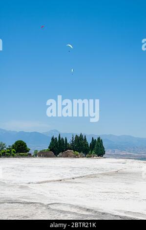 Paragliders flying above snow-white like Travertines of Pamukkale in ancient city of Hierapolis in Turkey. Stock Photo