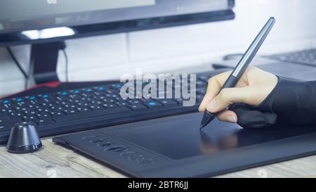 A woman's hand in a special glove draws on a graphic tablet. Freelance. Designer Illustrator draws comics, sketches. Digital tablet, visual, multimedi Stock Photo
