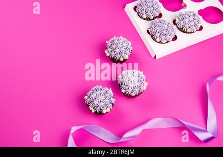 Delicious shawn cupcakes with curd cream in the form of flowers on a pink background. White cupcake packaging. Stock Photo