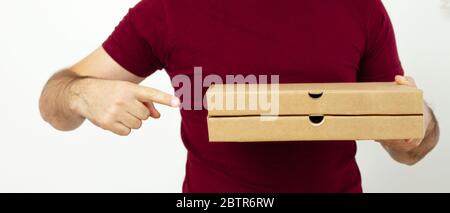 Delivery man in red t-short holding cardboard boxes of pizza on white background. Pizza delivery. Courier home delivery. food order pizza boxes Stock Photo