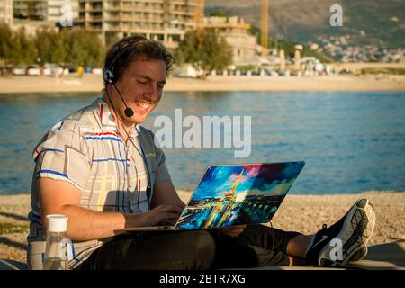 One man using laptop and headset outdoors at a beach Stock Photo