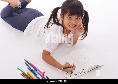 Cute little girl doing homework, reading a book, coloring pages, writing and painting. Children paint. Kids draw. Preschooler with books at home. Stock Photo