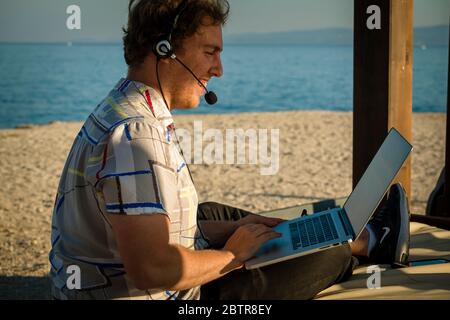 One man using laptop and headset outdoors at a beach Stock Photo