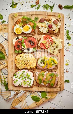 Colorful, different kinds sandwiches served on wooden chopping board. Vegetable toppings Stock Photo