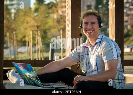 One man using laptop and headset outdoors at a beach Stock Photo