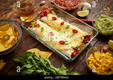 Vegetable Burritos served in glass heatproof dish. With salsa, guacamole, nachos and ingredients Stock Photo