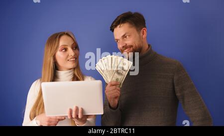 Young beautiful woman showing the bill on the tablet to her rich boyfriend who holds cash in his hands. Online shopping and relationship with interest. Stock Photo
