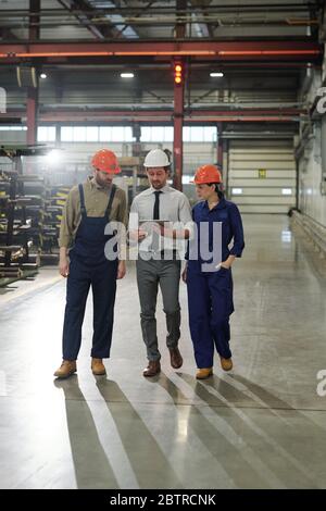 Industrial manager discussing production with workers while analyzing data on tablet and walking over workshop Stock Photo