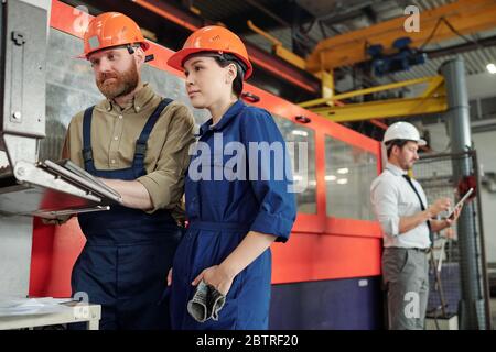 Professional of industrial plant explaining function of CNC machine to Asian worker in workshop Stock Photo