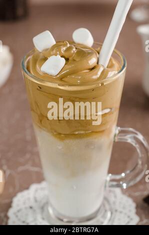 Cold coffee dalgon in a tall glass on a beige background close-up. Foam whipped with a mixer made of sugar, instant coffee and water in cold milk with Stock Photo