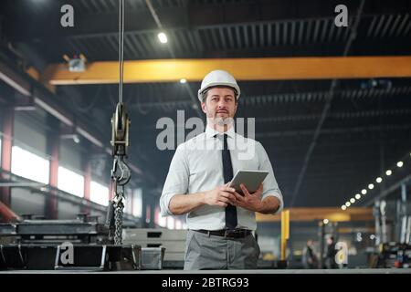 Portrait of qualified male technologist in shirt and tie standing with tablet in modern factory shop Stock Photo