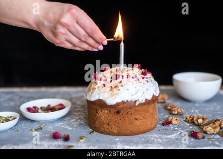The Easter cake is beautifully decorated and with a candle. White utensils on a concrete background. Stock Photo
