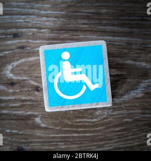 A blue disabled sign, symbol or icon for mentally disabled and physically disabled people on a wooden block with a wood background and copy space