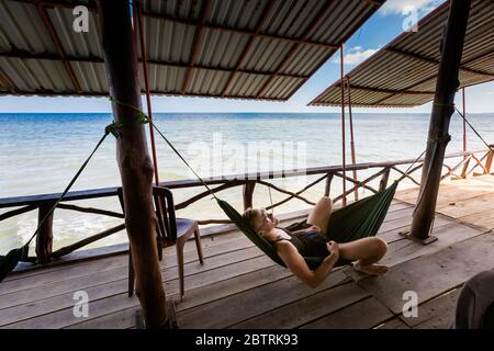 Young goodlooking man lying in a hammock in local seafood restaurant in  fishermans village Ham Ninh, tropical Phu Quoc island (Bai Thom area) in Viet Stock Photo