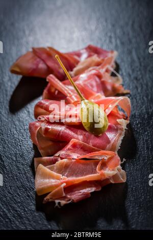 Delicious serrano ham with caper berries on black background Stock Photo