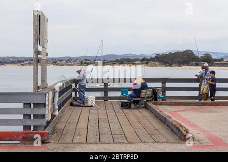 Monterey, California, USA- 09 June 2015: Anglers fishing on a wooden pier. Bay and mountain in the background. Stock Photo