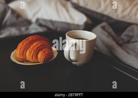 Breakfast on a tray in bed at home white dark linen. croissant tea strawberries. Stock Photo