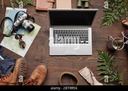 Flat lay composition symbolizing active tourism: laptop, maps, thermos mug, belt, compass on wooden table Stock Photo