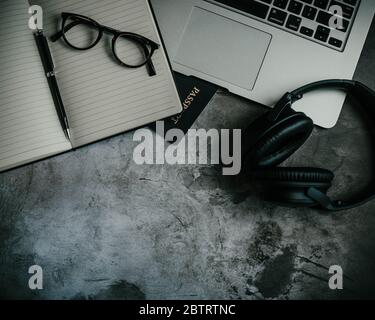 Image of an industrial flat lay design with an open notebook, glasses, passport, laptop, and black wireless headphones on a concrete background Stock Photo