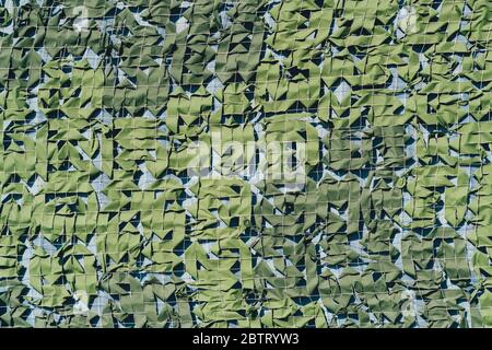 The texture of a camouflage mesh in shades of green with thin squares of a white net rope inside, bluish background Stock Photo