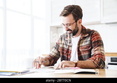 Portrait of excited bearded man wearing eyeglasses smiling while working with notes at home Stock Photo