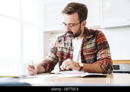 Portrait of young bearded man wearing eyeglasses working with notes at home Stock Photo