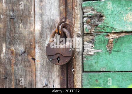 A old iron padlock hangs on the wood door. Locked door to the premise. Concept of protection, incarceration, protection, prison. Stock Photo