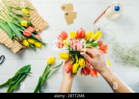Top view male florist hands making spring bouquet using tulips at workspace with recycled wrapping materials. Learning flower arranging. Education of Stock Photo