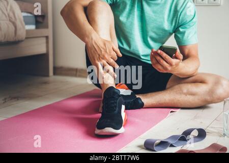Caucasian man working out from home is resting after doing morning exercises while looking at phone