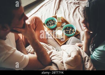 Lovely couple in bed looking at each other before eating cereals with milk in the morning Stock Photo
