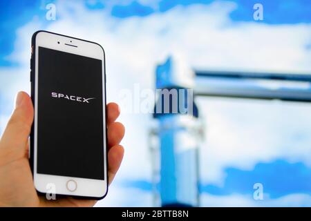 Kennedy Space Center, Florida, United States. May 27, 2020. A person holding a iPhone with the SpaceX logo with an out of focus rocket launch backgrou Stock Photo