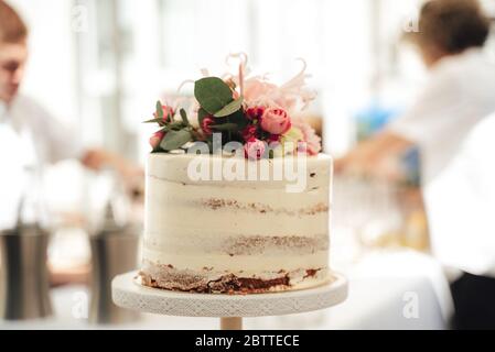 Close up sweet small round white cake on stand. Pink flower decoration on top. Celebration, party, birthday or wedding concept. Stock Photo