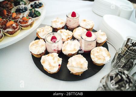 Mix of glasses with raspberry sweet dessert and various cupcakes on buffet table. Celebration, party, birthday or wedding concept. Stock Photo