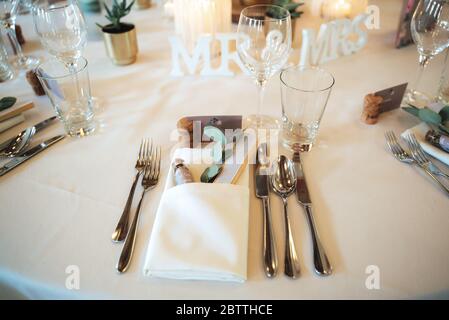 Elegant wedding table setting with cutlery, napkin and glassware on white table cloth. Each guest get small gift. Wedding day concept. Stock Photo