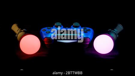 Blue Playstation 4 controller with Move controllers lit up against a black background. Stock Photo