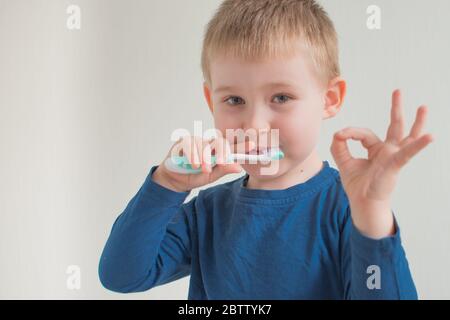 Portrait of little boy brushing teeth on light background and show ok sign. Dental hygiene. Copy space for text Stock Photo