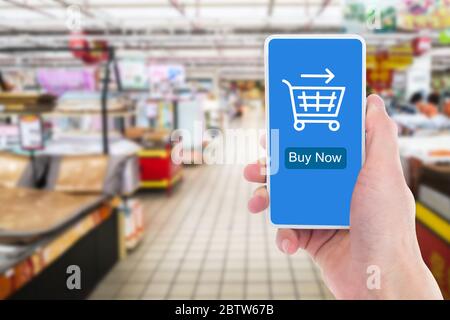 In the supermarket, close-up of a man's hand holding a mobile phone to shop online. Stock Photo