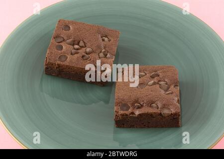 Two chocolate chip brownie squares on blue plate on pink background Stock Photo