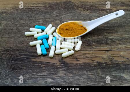 Colorful pill and yellow turmeric powder in ceramic spoon on grunge wooden background. Stock Photo