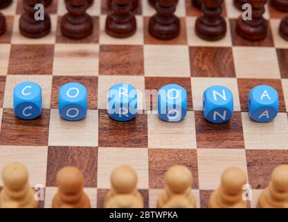 Chess piece pawn black and white, face each other on a small chess board, in the middle there are letter cubes, which form the word Corona. Stock Photo