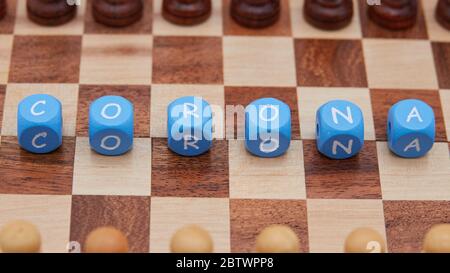 Chess piece pawn black and white, face each other on a small chess board, in the middle there are letter cubes, which form the word Corona. Stock Photo