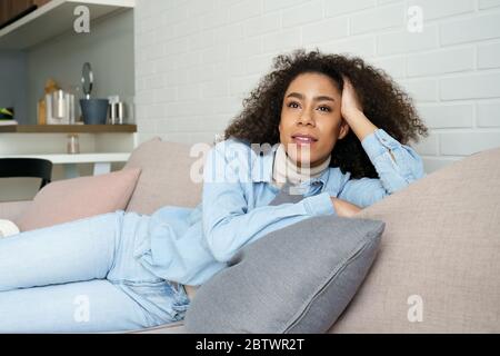 Serene relaxed african woman lounge on comfortable sofa, dreaming at home. Stock Photo
