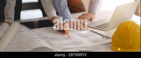Cropped shot of two engineers working together with blueprint, laptop and tablet on white desk Stock Photo