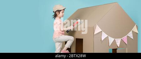 Asian little child girl building her cardboard house isolated on blue long banner with copy space for your text, Creative at home with family concept Stock Photo