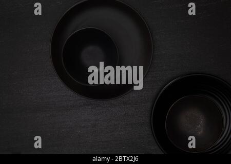 Group of empty blank black ceramic round bowls and plates on black stone blackground, Top view of traditional handcrafted kitchenware concept Stock Photo