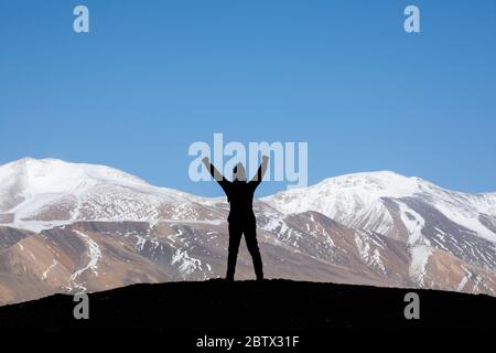 Silhouette of woman hiker stands on the rock in the beautiful mountains view of snowy Tso Moriri Lake in Leh Ladakh india, success concept Stock Photo