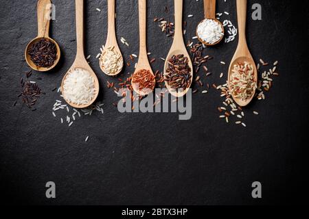 White rice, Jasmine rice, Black rice, Brown rice, Riceberry and Mixed rice in wooden spoon over black table background with copy space  for your text, Stock Photo