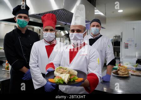 Mixed race team Portrait of group chefs standing together in the kitchen at restaurant wearing protective medical mask and gloves in coronavirus new n Stock Photo