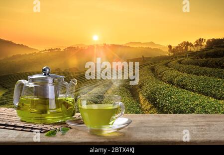 Green Tea cup and glass jugs or jars. with and Green tea leaf sacking on the wooden table and the tea plantations background Stock Photo