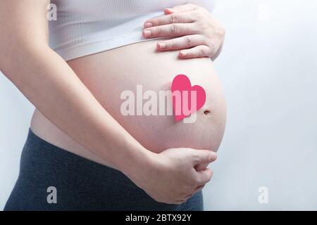 Pregnant woman with single pink heart on her baby bump. All on white background. Stock Photo
